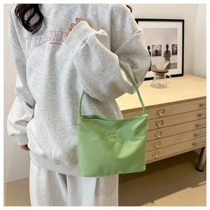 Détail du sac à bandoulière vert en tissu avec broderie porté sur un sweat à capuche gris