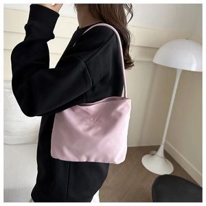 Détail de la broderie sur un sac à épaule en nylon rose porté par un mannequin
