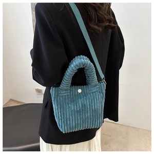 Blue corduroy bucket bag with twisted handle and wide strap on model back view