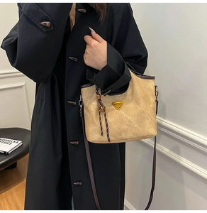 Detail showing the beige canvas bucket bag with gold triangle logo and braided pendant