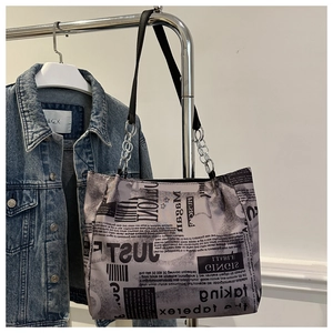 Dettaglio borsa tote con stampa giornale, anelli metallici argento e tracolle nere