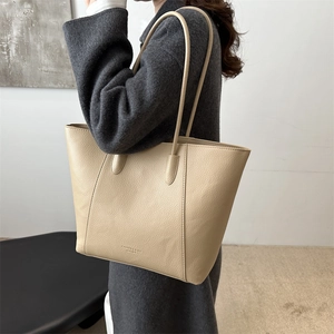 Large beige leather tote bag with lychee texture worn over a dark grey wool coat