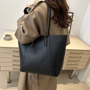 Minimalist black oversized leather tote bag shown on a model wearing a khaki trench coat