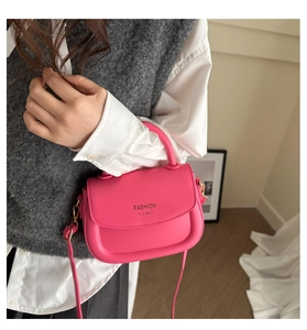Detail of bright pink leather saddle bag with gold lettering and metallic side hooks