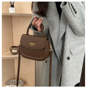Close-up of brown faux leather saddle bag held by model wearing a grey blazer