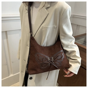 Détail du sac à bandoulière en daim marron foncé avec patch papillon en cuir