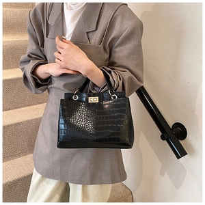 Elegant black crocodile pattern handbag with gold hardware shown in a lifestyle setting