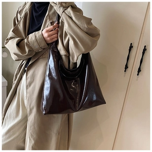 Detail of a large dark brown high-gloss oil wax leather tote bag worn by a model