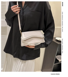 Close-up of minimalist beige crossbody bag with textured flap and golden hardware detail