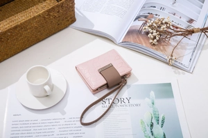 Pink quilted short wallet with wrist strap near coffee and magazine on table