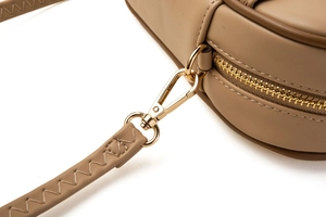 Détails du zip doré et de la bandoulière tressée en cuir sur un sac bandoulière beige