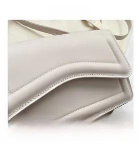 Macro detail of beige leather crossbody bag featuring unique wavy stitching and edge finish