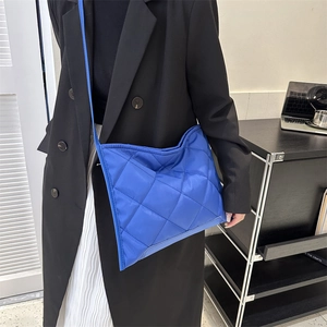 Gesteppte blaue Umhängetasche mit Rautenmuster, präsentiert von einem Modell im Raum