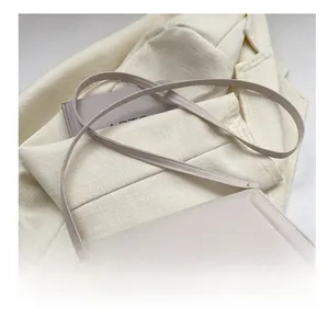 Close-up of beige leather shoulder bag with adjustable gold buckle on a white blazer
