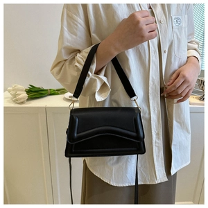 Detail of black crossbody bag with V-shaped stitching and golden metal hardware on model