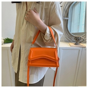 Detail of orange crossbody bag featuring geometric embossed texture and top handle