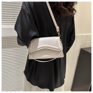 Detail of cream crossbody bag featuring wavy flap design and gold hardware on model