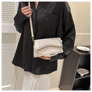 Minimalist beige crossbody square bag with wavy flap shown on a model in elegant outfit
