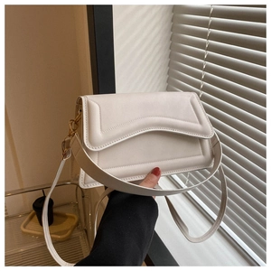 Detail of a cream-white square crossbody bag featuring a unique wavy flap design