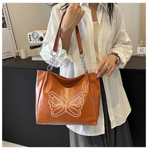 Detail of tan leather tote bag with white butterfly pattern and metal chain strap