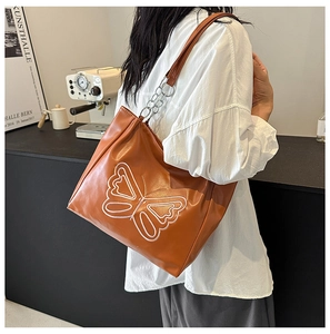 Detail of orange faux leather tote bag featuring white butterfly embroidery and metal chain strap