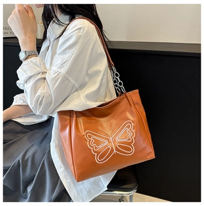 Detail of a brown tote bag featuring a white butterfly pattern and chain shoulder strap