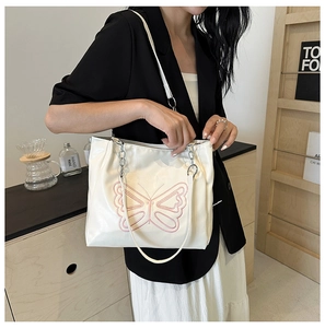 Close-up of cream tote bag with pink butterfly embroidery and metal chain strap