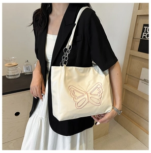 Close-up of cream tote bag featuring pink butterfly embroidery and chain strap detail