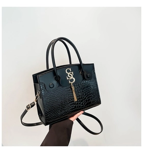 Détail du sac à main noir motif crocodile avec boucle dorée et pampilles métalliques