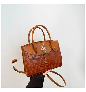 Détail du sac à main marron motif crocodile avec logo S et pendentif à franges