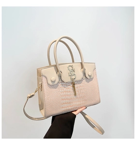 Détail du cuir gaufré crocodile et du logo S doré avec pompon sur le sac à main beige