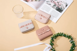 Three compact square zip wallets with elegant ribbon trim on a warm lifestyle background