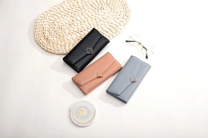 Three leather wallets in black, pink, and blue with gold clover buckles on a white table