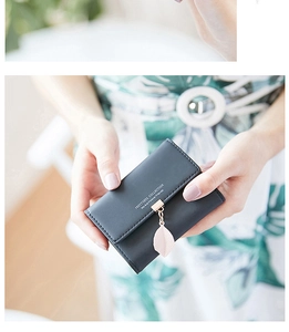 Detail of a dark gray leather wallet featuring a unique leaf pendant and gold clasp