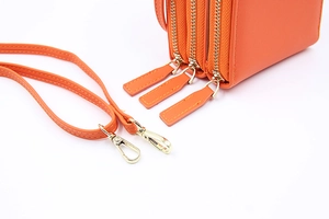 Détail du sac de téléphone orange avec trois fermetures éclair et ferrures dorées
