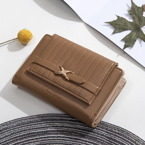 Detailed close-up of brown textured leather wallet with gold metal X-clasp and zip compartment