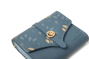 Detail of grey-blue leather wallet showing printed leaf patterns and leaf-shaped metal buckle