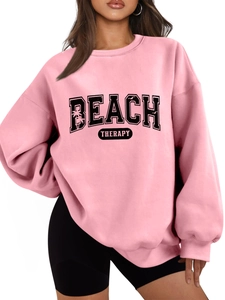 Close-up of pink oversized sweatshirt featuring black BEACH THERAPY text with palm trees