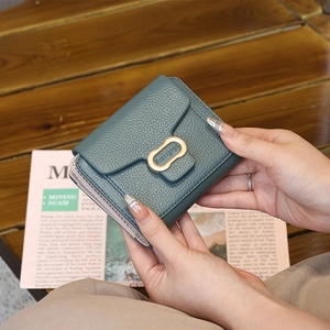 Close-up of green pebble leather wallet with gold metal logo clasp held by hands