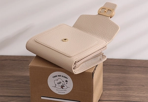 Detail of beige lychee grain leather wallet with gold metal logo buckle and zipper