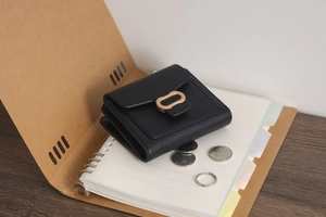 Detail of black pebbled leather wallet featuring a gold oval clasp and neat edge stitching