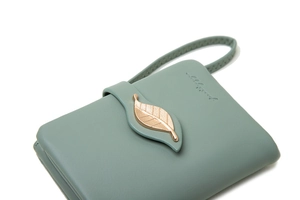 Macro shot of light green leather wallet featuring a gold leaf buckle and wrist strap