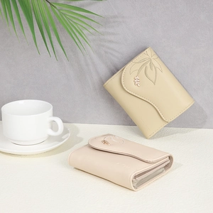 Detail of short fold PU wallet featuring floral embroidery and metal leaf pendant
