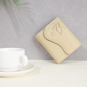 Detail of elegant beige wallet featuring intricate leaf embroidery and gold metal leaf ornament