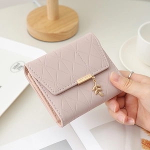 Detailed view of pink quilted short tri-fold wallet with elegant gold leaf pendant charm