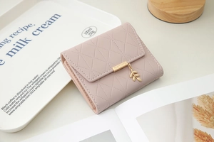 Detail of pink quilted tri-fold wallet featuring a golden leaf pendant and buckle
