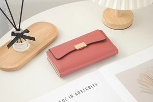 Portefeuille long en cuir rose poudré avec boucle dorée sur un fond lifestyle minimaliste