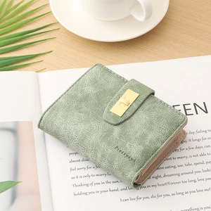 Close-up of sage green leather wallet with gold metal clasp on a lifestyle background