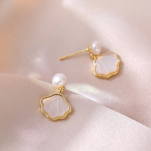 Golden fan-shaped shell earrings with white pearls on elegant champagne silk fabric