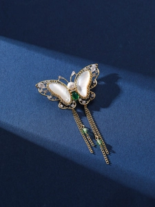 Macro detail of butterfly brooch with shell wings, pearls and dangling golden tassels
